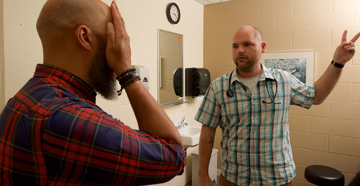 Photograph of a male nursing student checking the vision of a male nursing instructor in a replicated patient room within Metro State’s Simulation Center on the Saint Paul Campus.