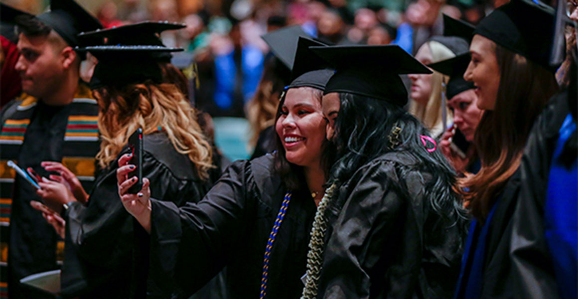 Metro State University happy graduates smiling and taking selfies of themselves in graduation regalia at Fall commencement 2019.