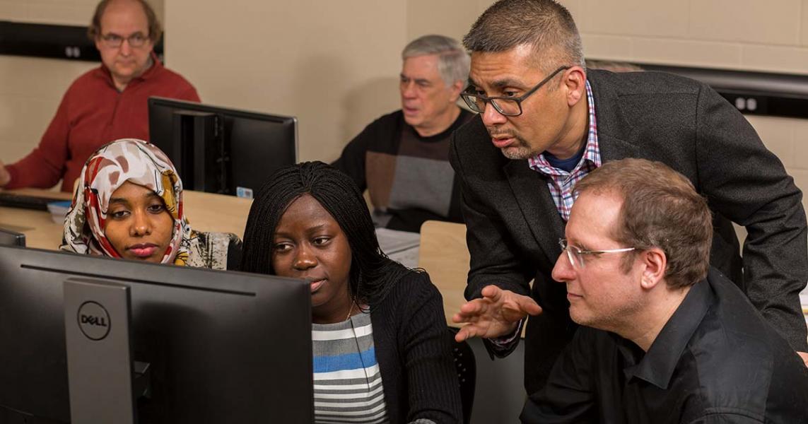 A group of people of different ages and ethnicities are looking at a computer screen.