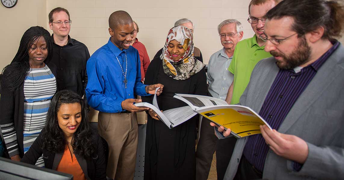 Several students stand in a semicircle looking at open books.