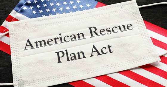 White medical mask with the words "American Rescue Plan Act" printed on it, lying flat on top of an American flag