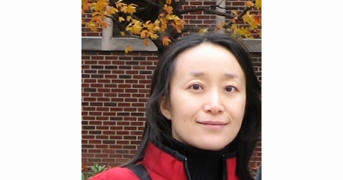 A woman in a red jacket smiles in front of a brick wall