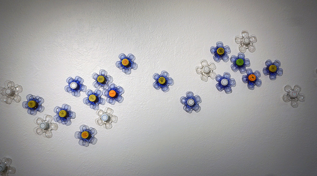 plastic bottle bottoms arrayed against a white wall, with plastic bottle caps in the center of each, to resemble flowers