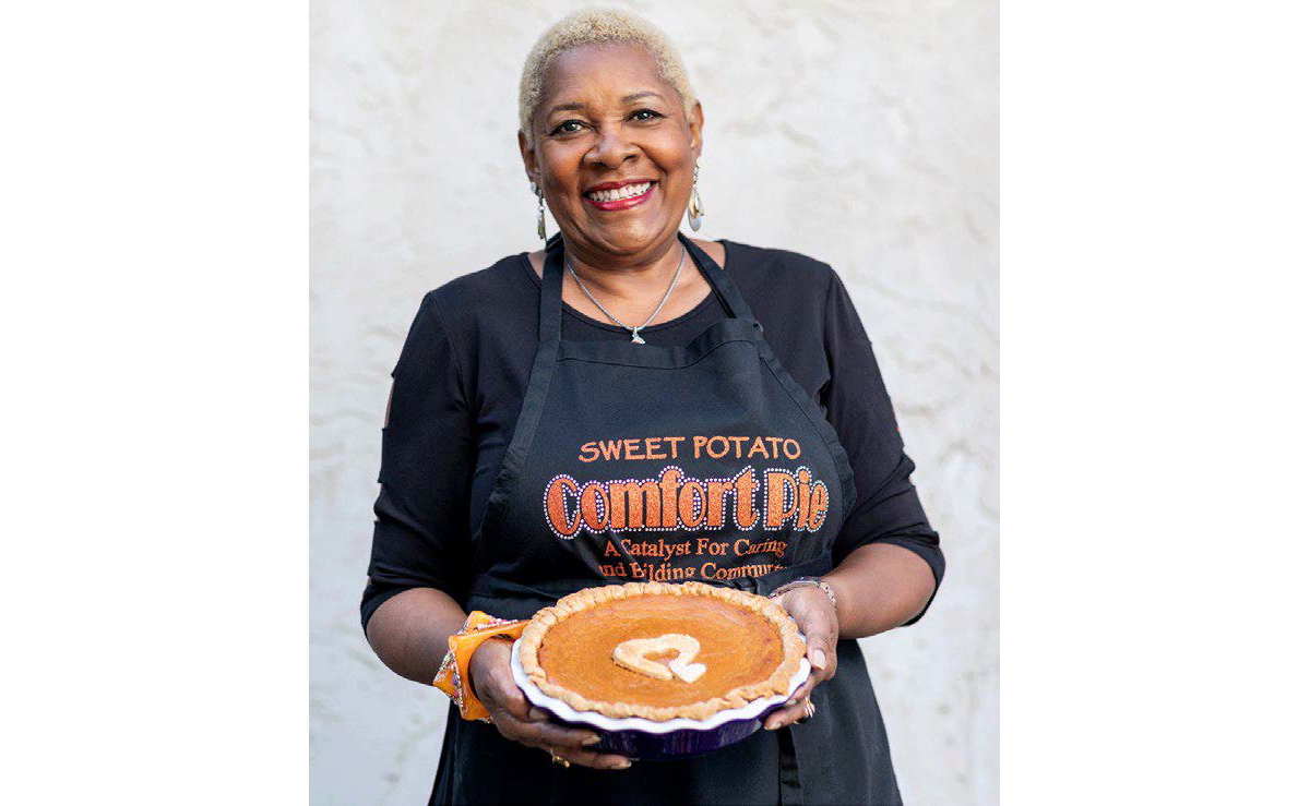 A person wearing a dark apron holding a sweet potato pie.