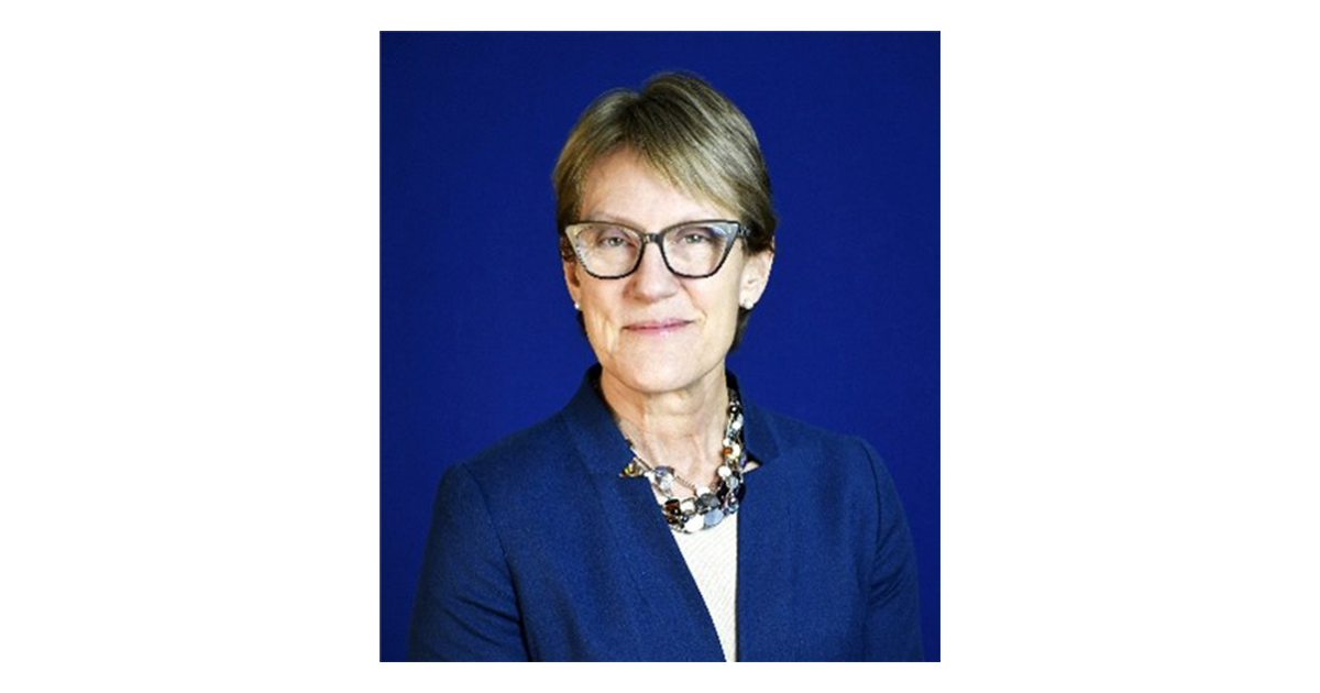 A person sits for a portrait against a blue backdrop
