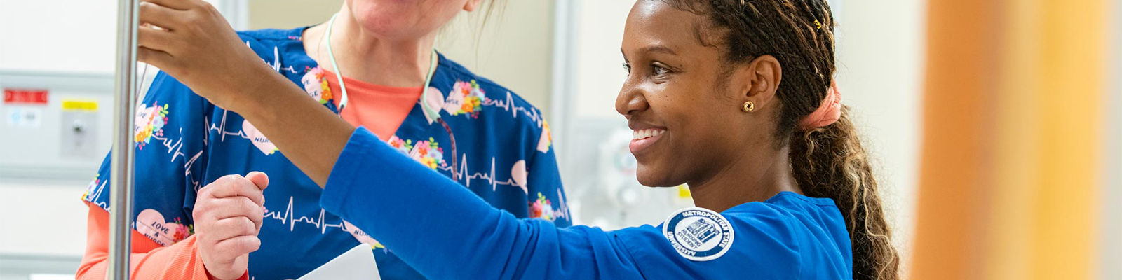 Nursing student working in the Nursing Simulation Lab, hanging an IV with the assistance of a faculty member.