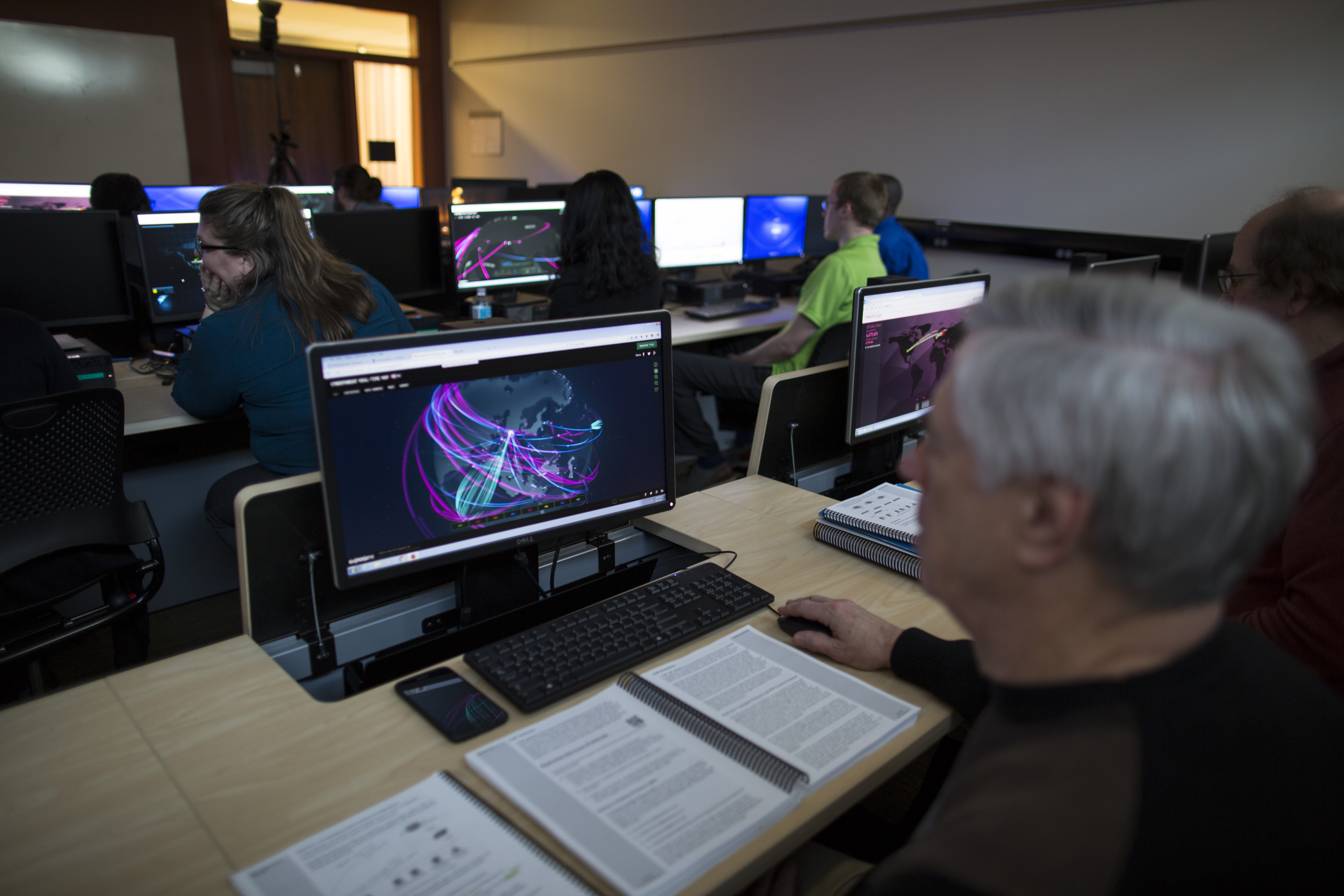 an individual looks at a computer screen, with several others in a classroom beyond doing the same thing