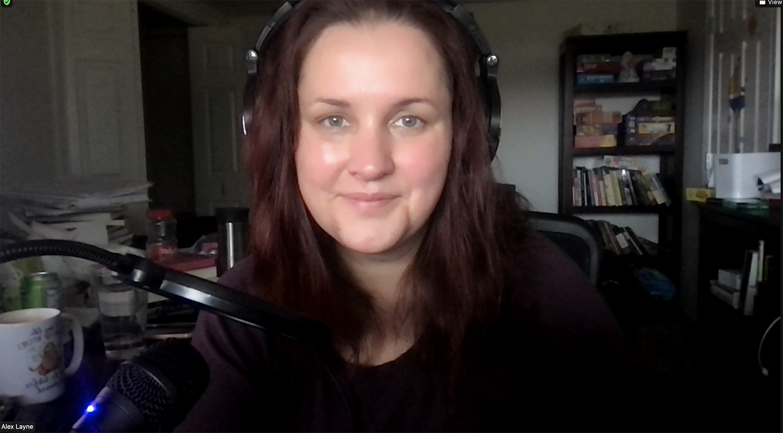 A woman wearing headphones looks directly at the viewer from a darkened room