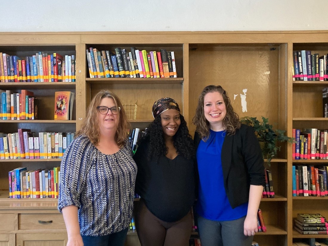 Three women stand in front of a bookshelf