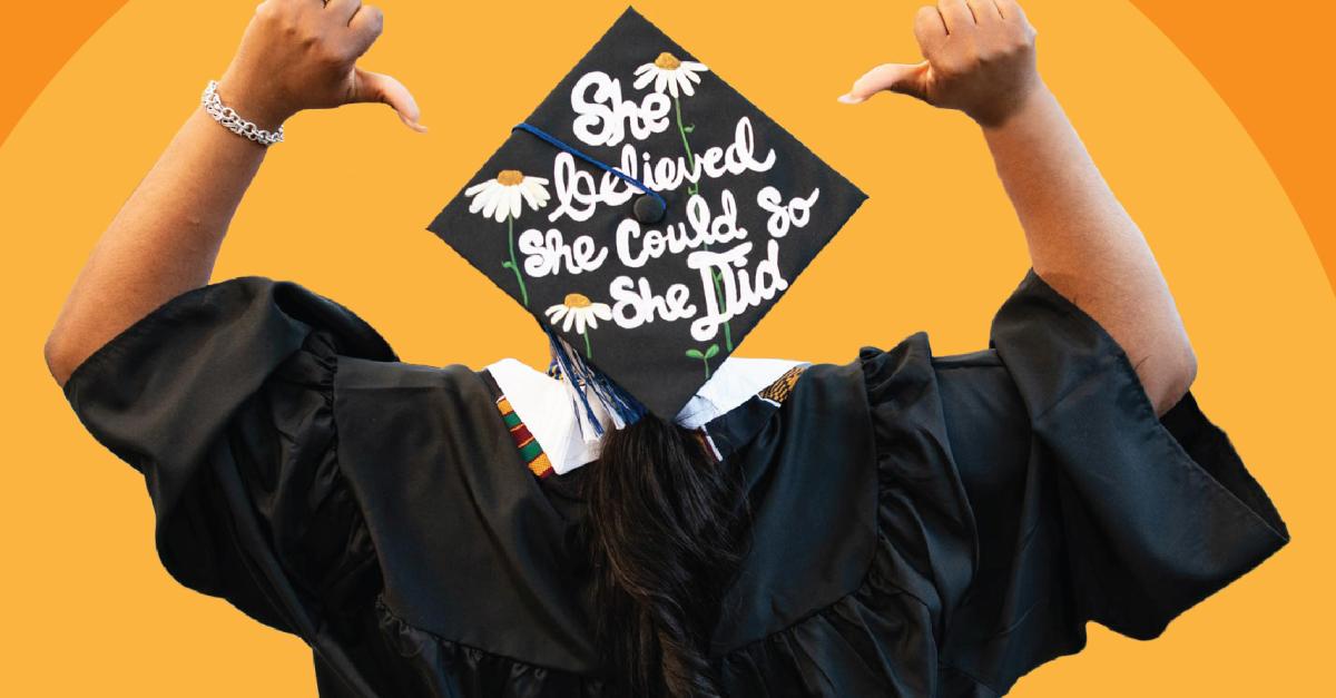 Against an Orange background, a person in cap and gown facing away from the camera, pointing to the cap which says "She believed she could, so she did."