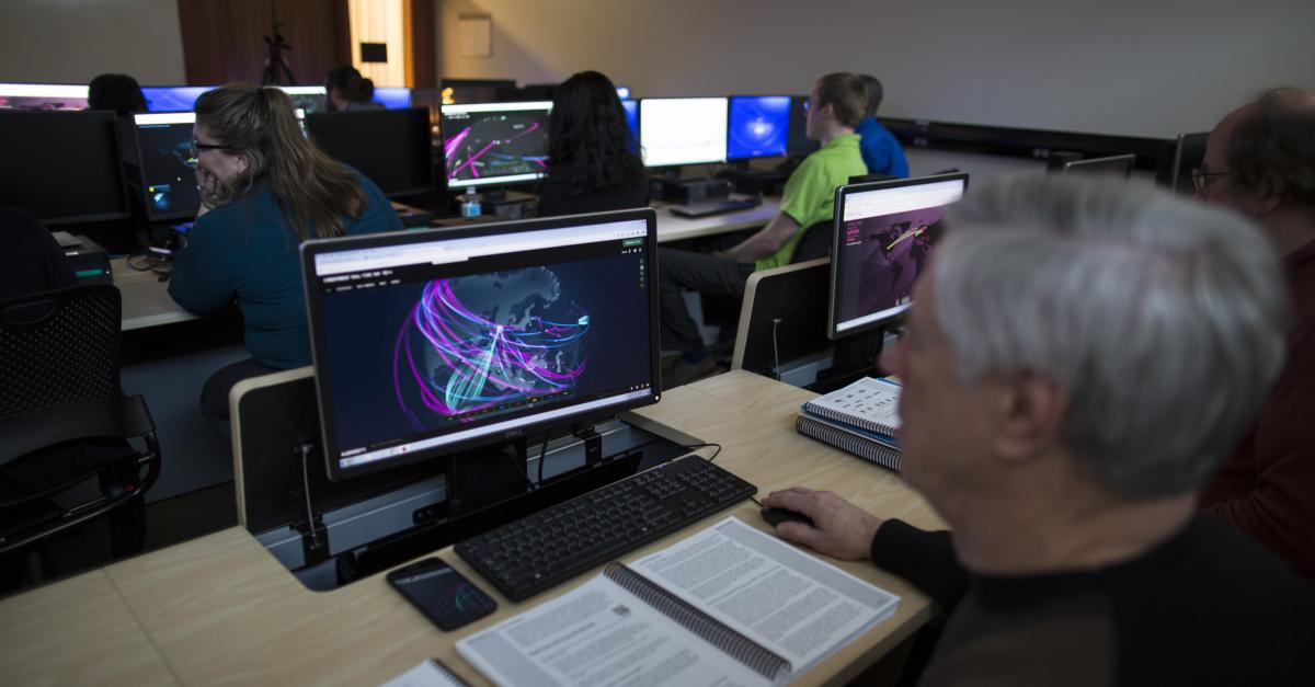 an individual looks at a computer screen, with several others in a classroom beyond doing the same thing