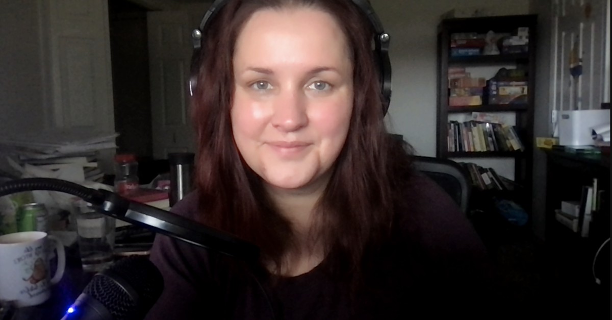 A woman wearing headphones looks directly at the viewer from a darkened room