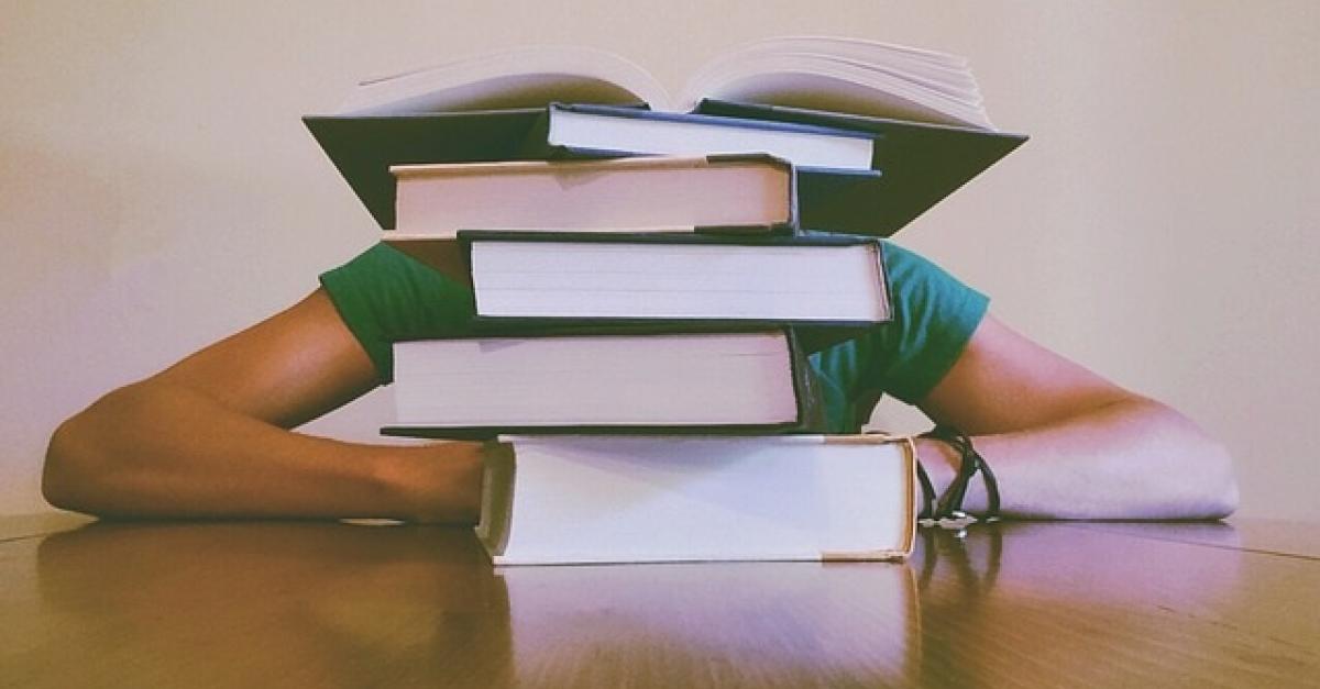 A person's elbows behind a stack of books.