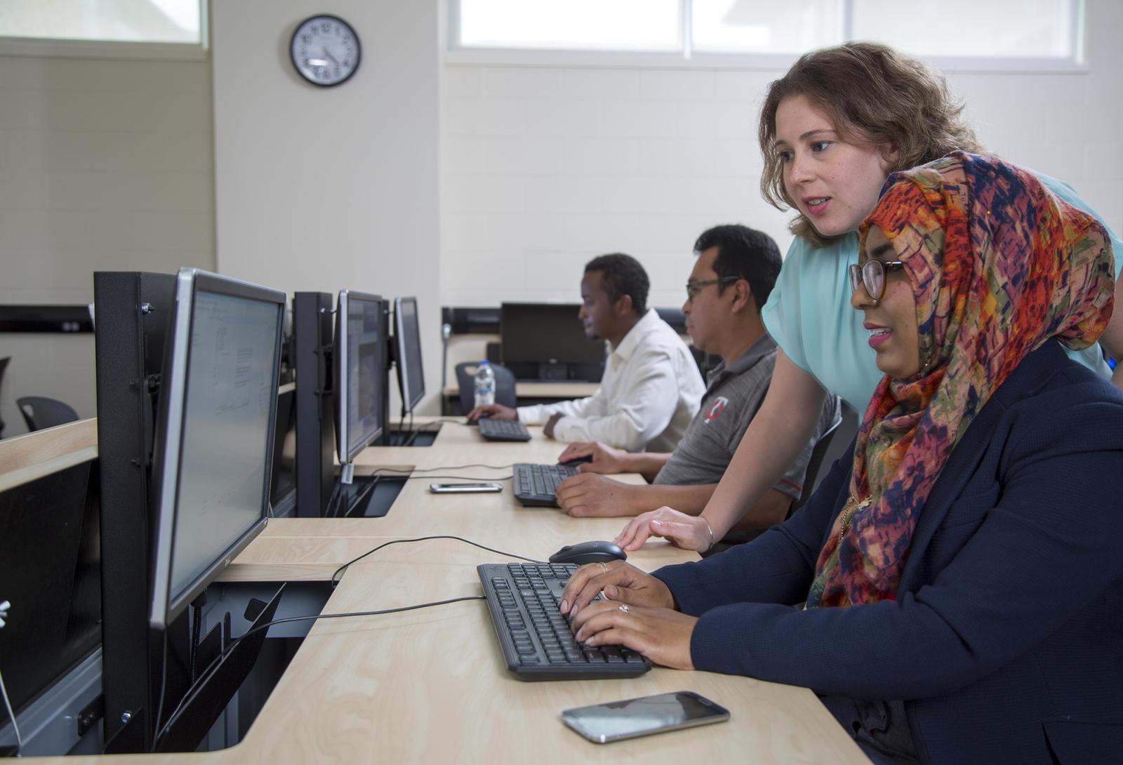 Instructor helping student in front of computer screen
