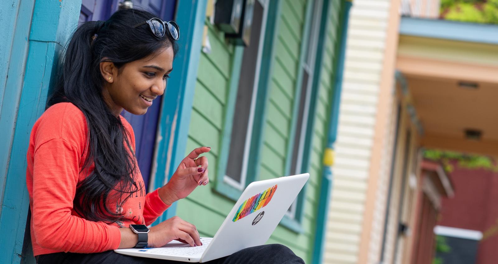 a woman sitting and working on a laptop computer in front of a blue and green house