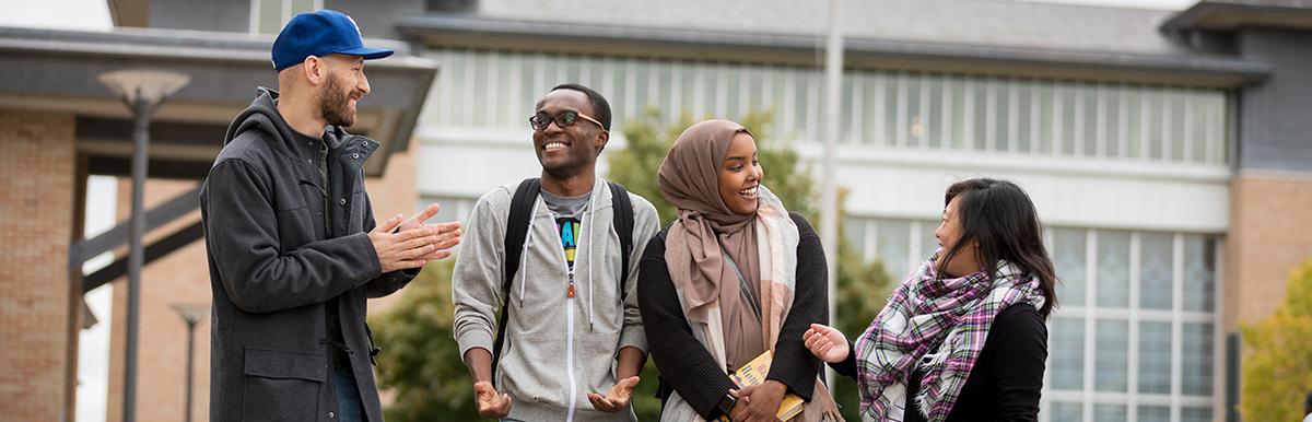 A group of students conversing outside in front of Founders Hall with New Main in the background