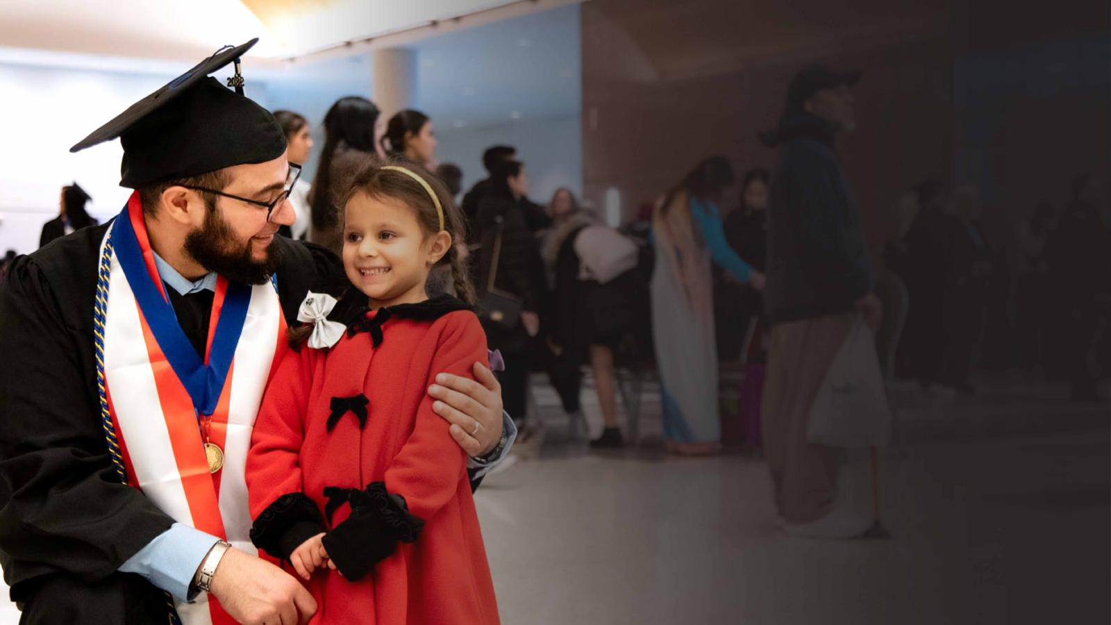 A person in cap and gown kneeling and hugging a child in a bright red coat