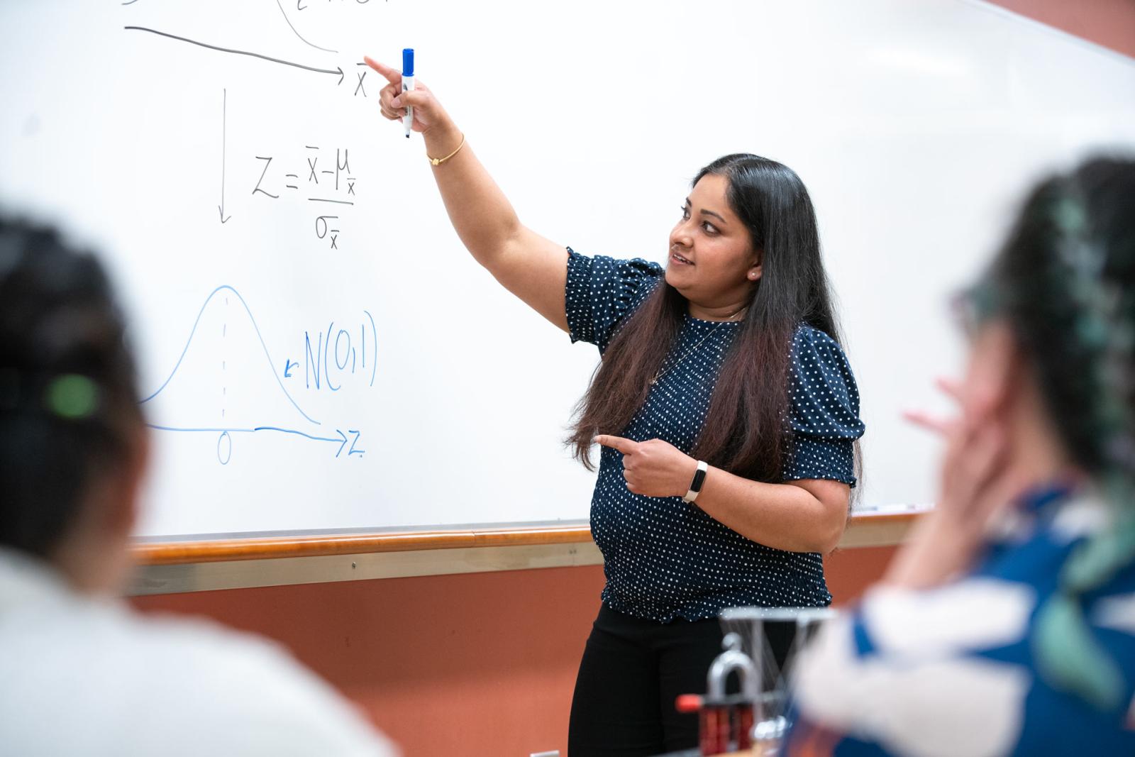 an instructor points to notes on a whiteboard as students look on