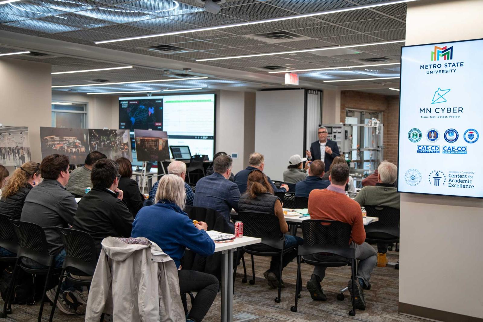 A large classroom of people listens to a speaker