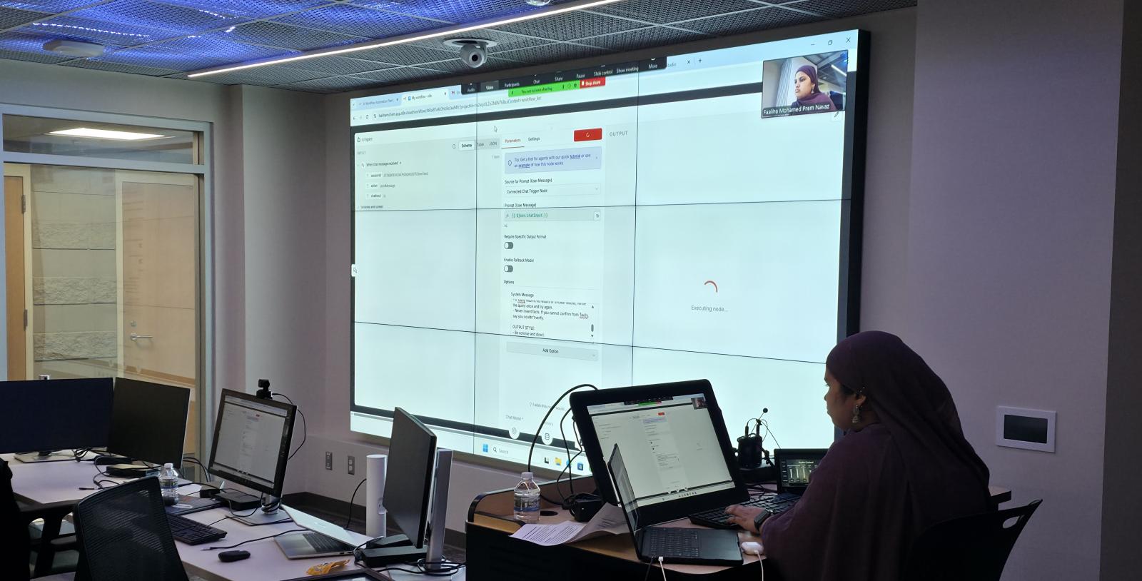 a person sits at a computer in front of a large screen displaying the work they are doing