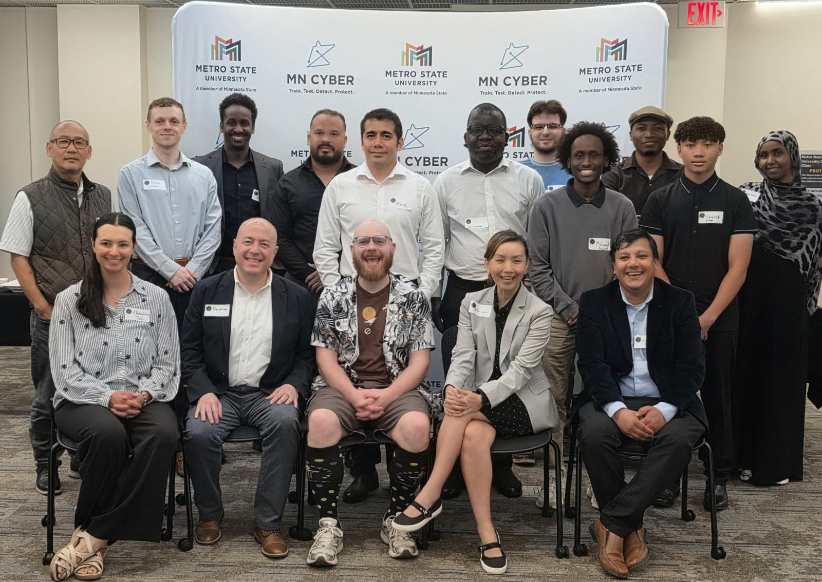 A group of people pose for a photo in front of the Metro State MN Cyber backdrop