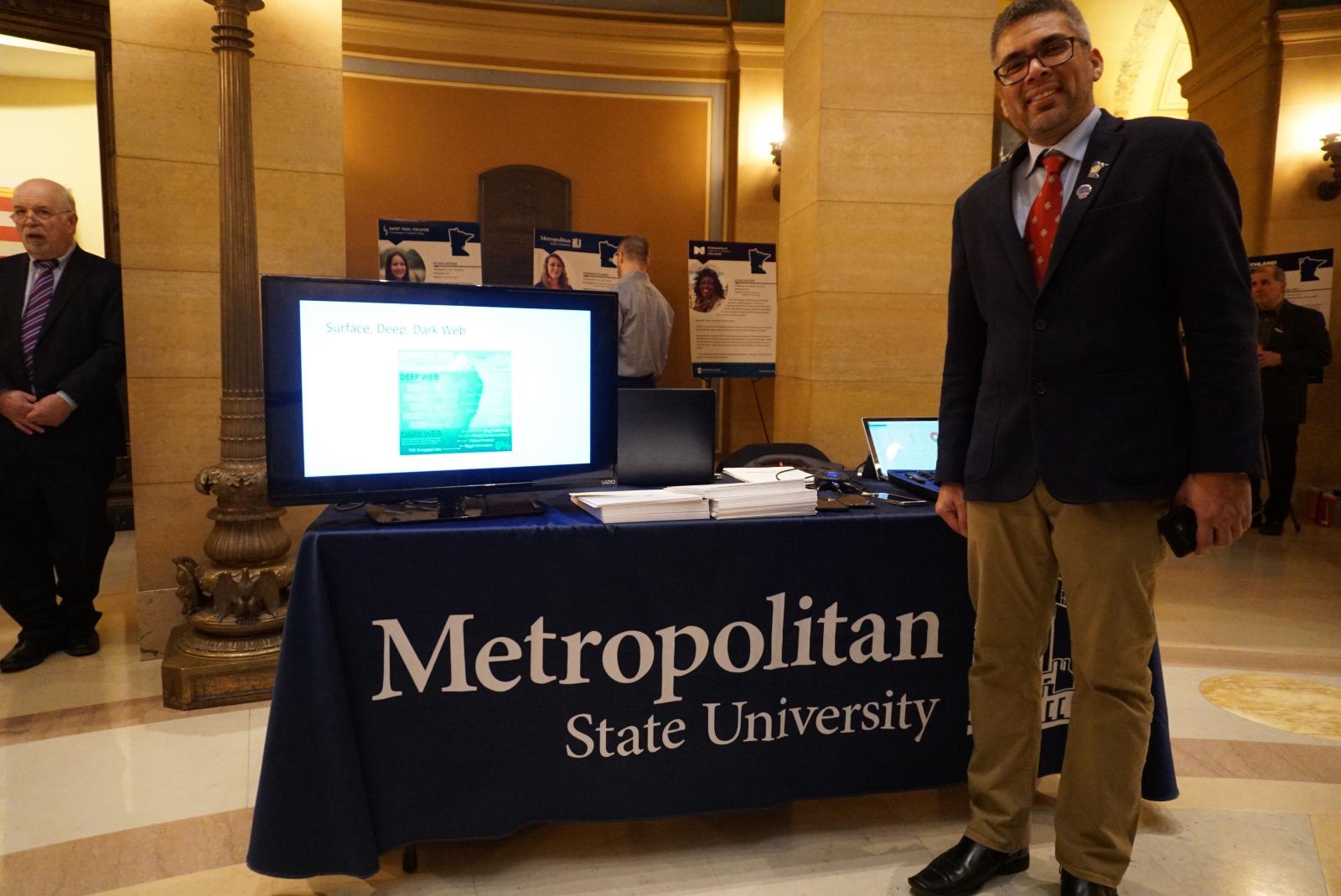 Faisal Kaleem of Metro State/s Computer Science and Cybersecurity program, stands in from of a table in the Minnesota State Capitol rotunda