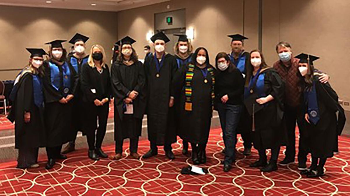 A group of students in cap and gown wearing protective face coverings