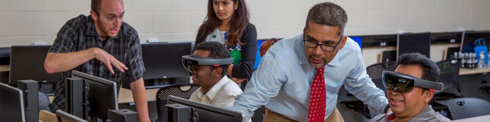 Professor in front of computer monitors with students