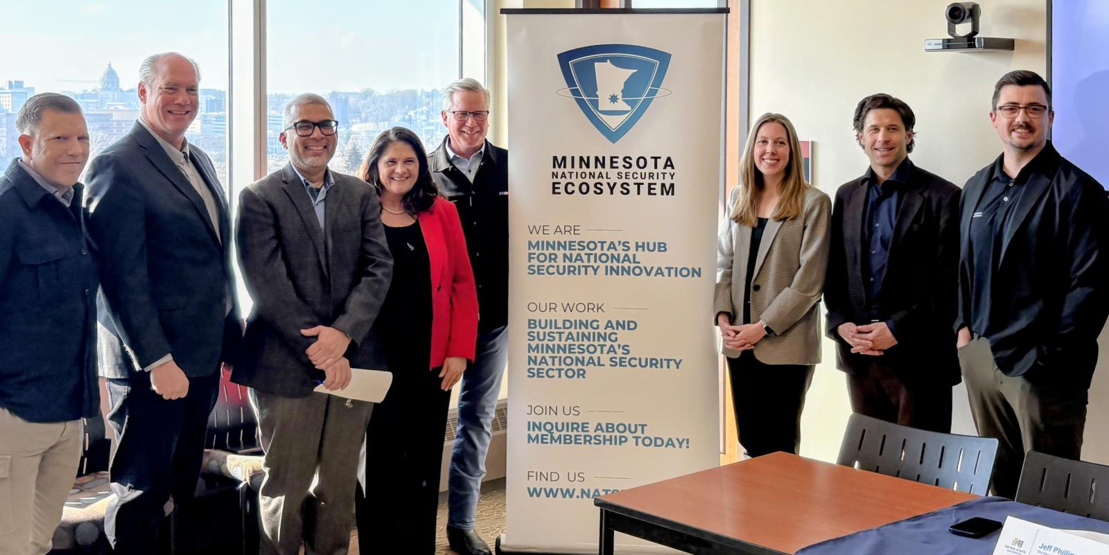 A group of people pose around Minnesota National Security Ecosystem pop-up banner