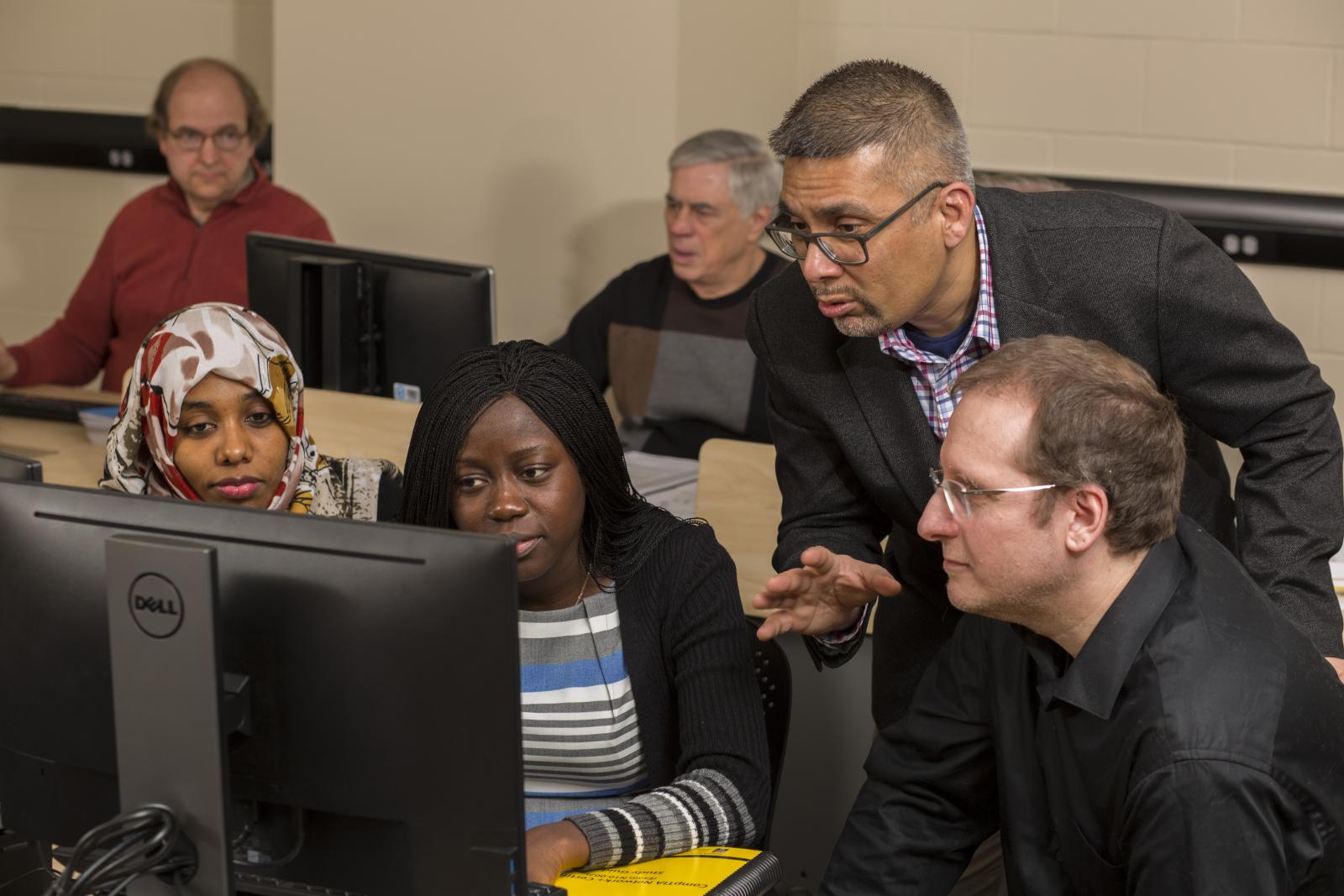students and a faculty member work together in a computer lab