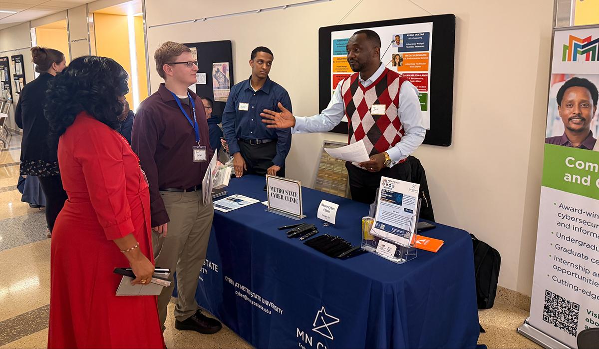 A group of people talking near the Cyber Clinic table at Diversity Networking and Job Fair