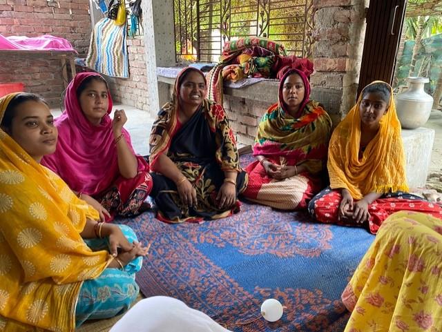 a group of people sitting on a blue and red rug wearing bright clothing