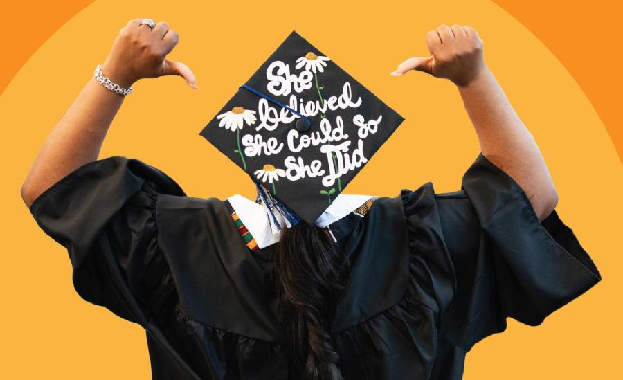 A person turned away from the camera, pointing to a mortarboard with both thumbs that reads, "She believed she could so she did."