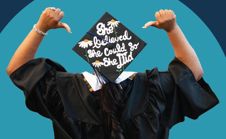 A person turned away from the camera, pointing to a mortarboard with both thumbs that reads, "She believed she could so she did."