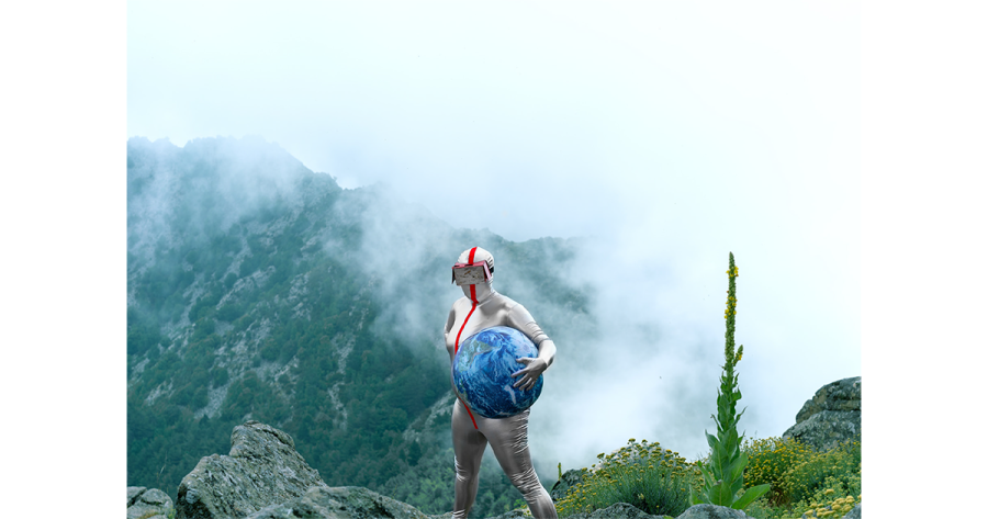 A person in a silver bodysuit and goggles holds a planet beach ball standing before a misty mountain valley