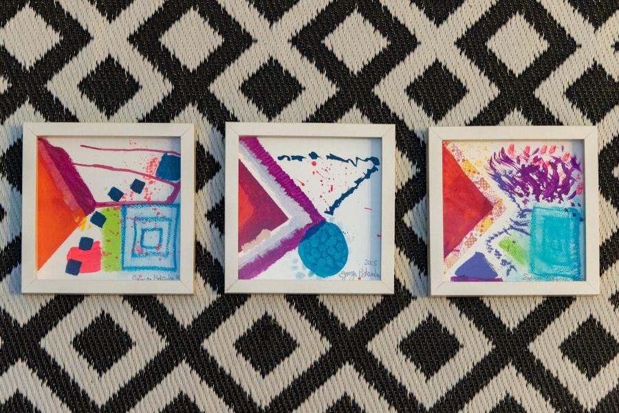 Three colorful square abstract paintings arranged against a patterned woven rug