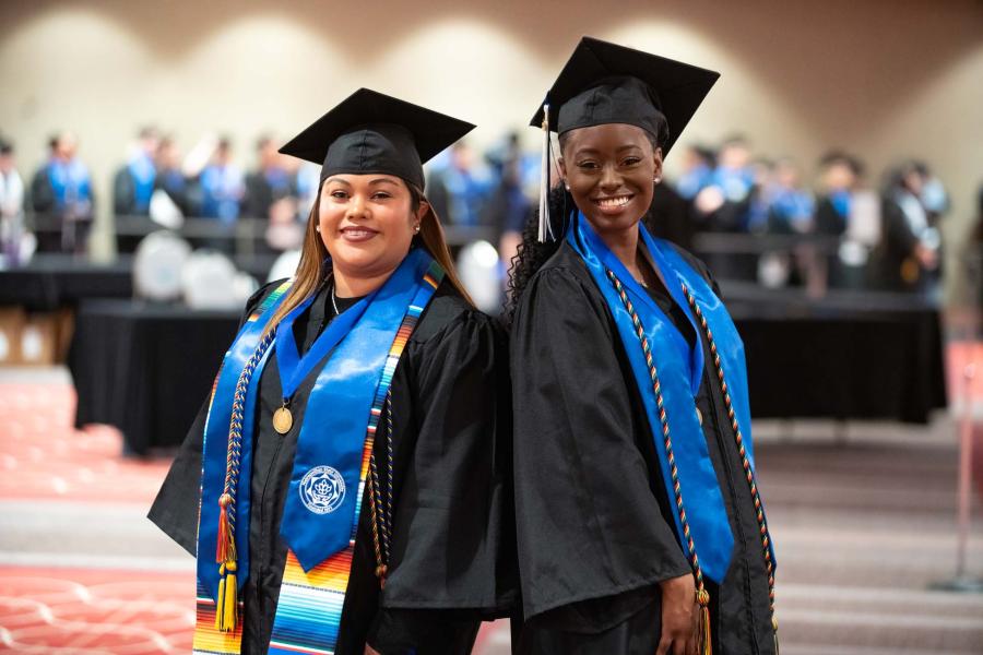 Two women in cap and gown pose at a commencement ceremony