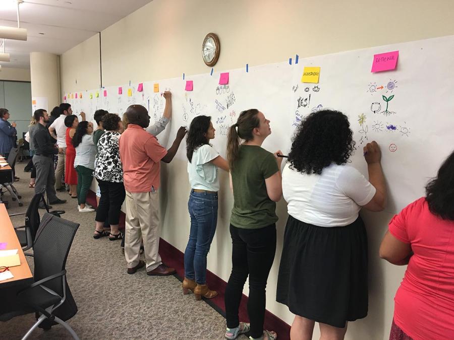 A number of people writing notes on wall-mounted notepads