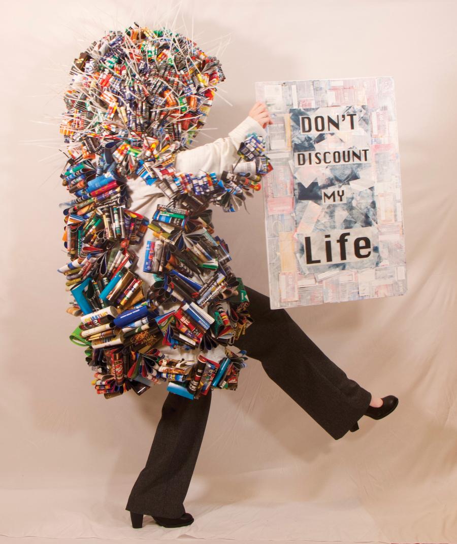 Artwork called Don't Discount My Life, featuring a person covered in a coat of coupons holding a poster that says Don't Discount My Life!