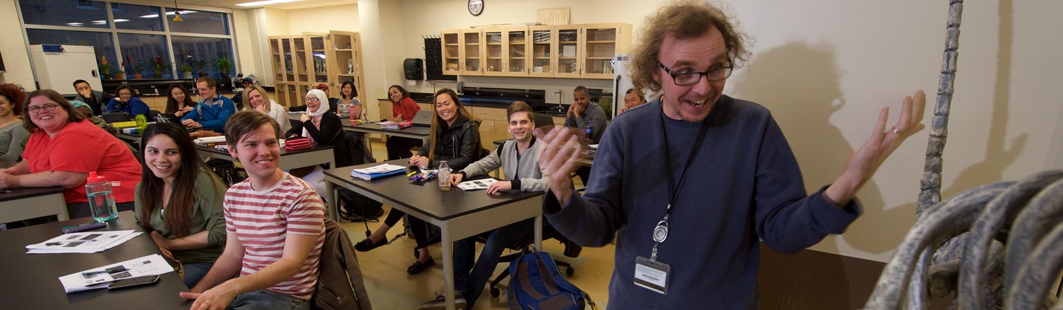An instructor, looking at a skeleton, gestures excitedly as smiling students listen.