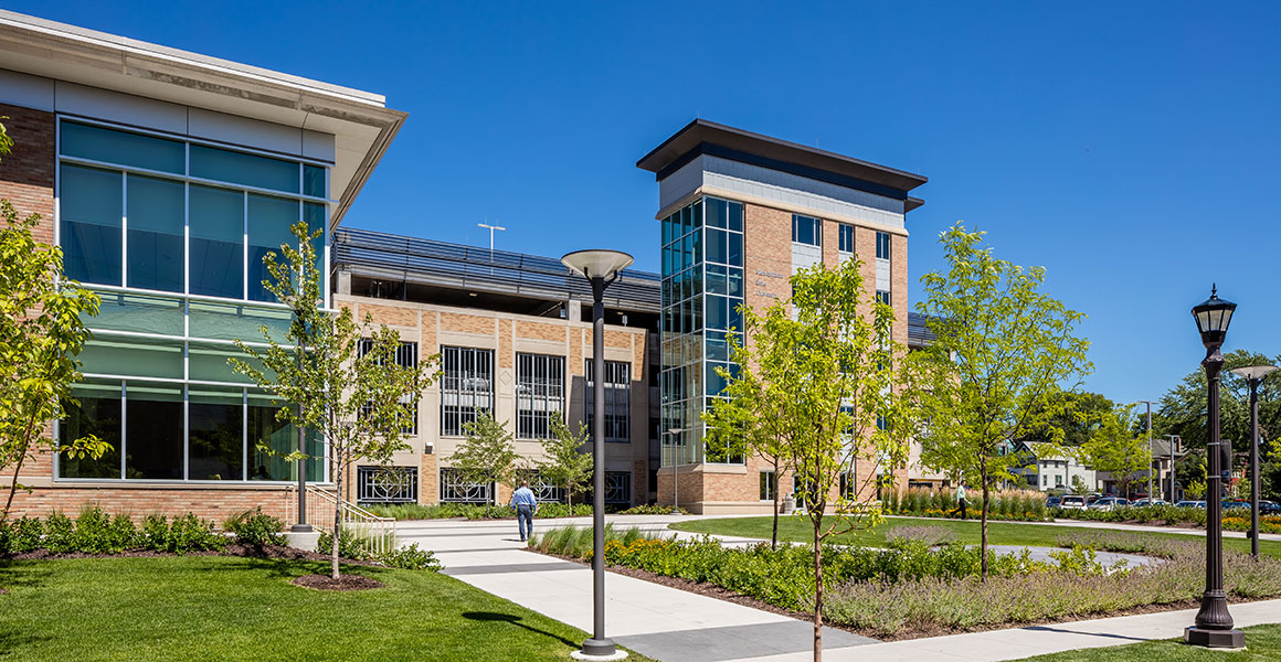 Metro State University’s Saint Paul campus parking ramp and adjacent buildings on a bright, cloudless summer day, with landscaped walkways and trees in the foreground.