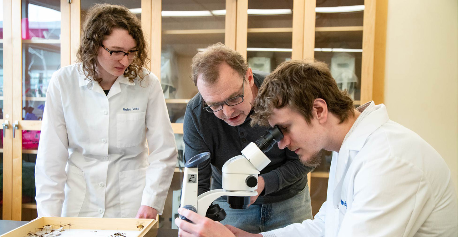 A faculty member and two students examine specimens with a microscope in a Metro State science lab.