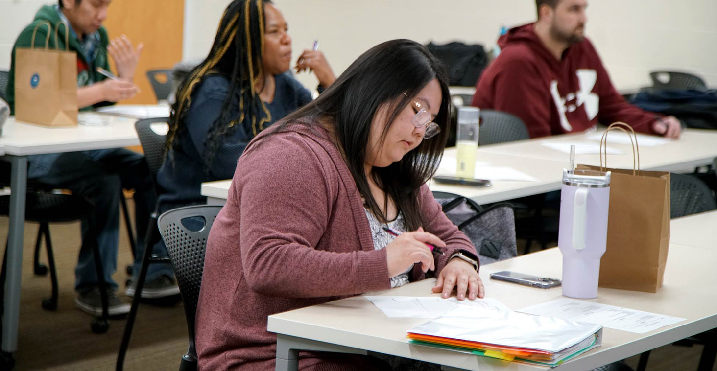 A student works on course materials in a Co-occurring Disorders Recovery Counseling classroom, with classmates seated nearby.